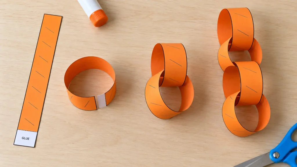 Halloween paper chain craft assembly showing an orange strip, an open loop, two linked rings, and a four ring body chain.
